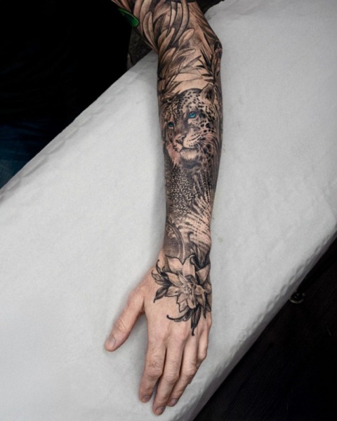 Jungle Realism: This powerful full-sleeve project by Lubava features a high-contrast leopard with piercing blue eyes and a seamless flow into a custom hand-piece.