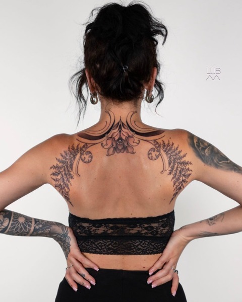 Anatomical Grace: This bespoke symmetrical back piece by Lubava features intricate fine-line ferns and ornamental floral details, designed to flow with the natural curve of the shoulders.